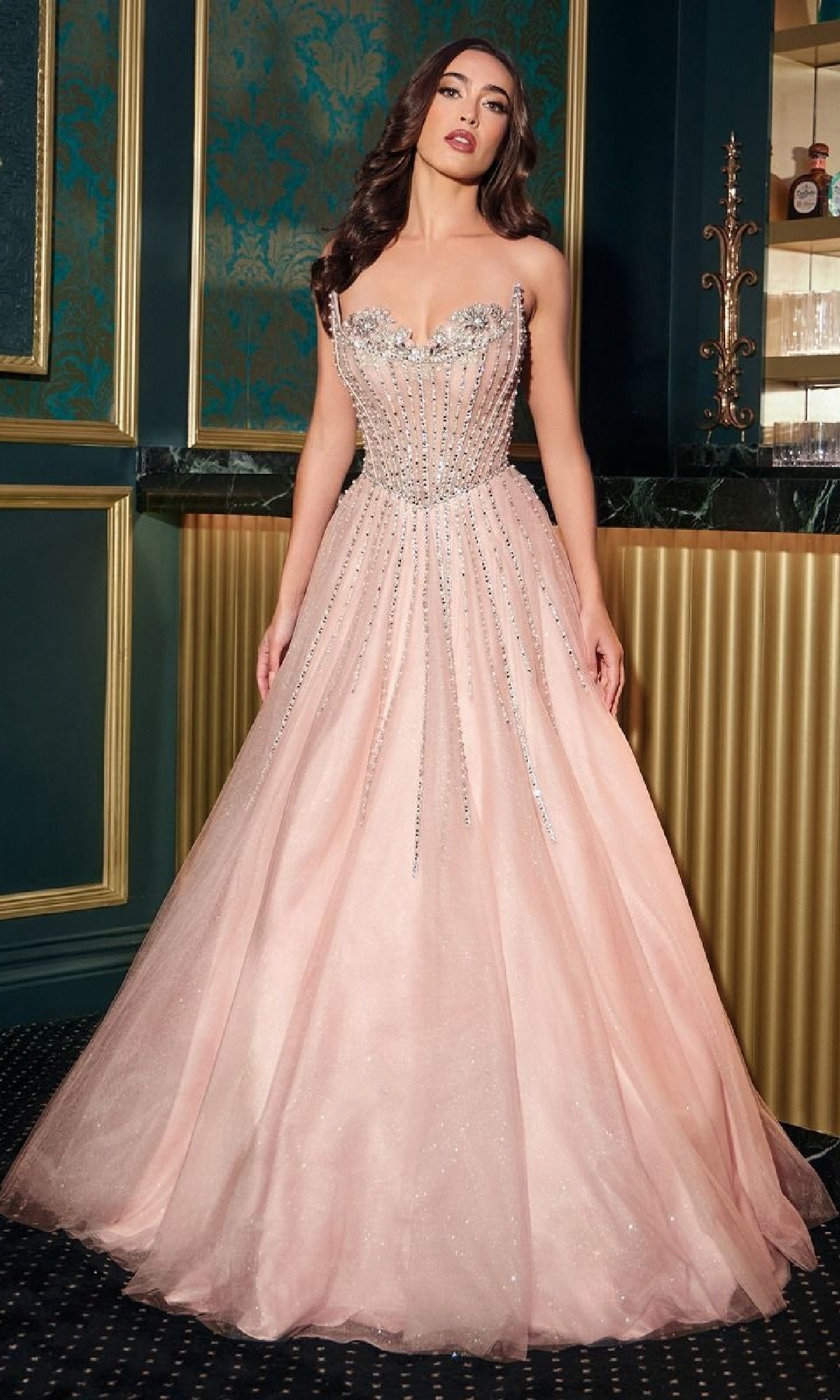 A woman stands indoors wearing the Ladivine CDS541 Strapless Beaded Prom Ball Gown in light pink, featuring a full tulle skirt and elegant bodice—an exquisite long formal dress for any special occasion.
